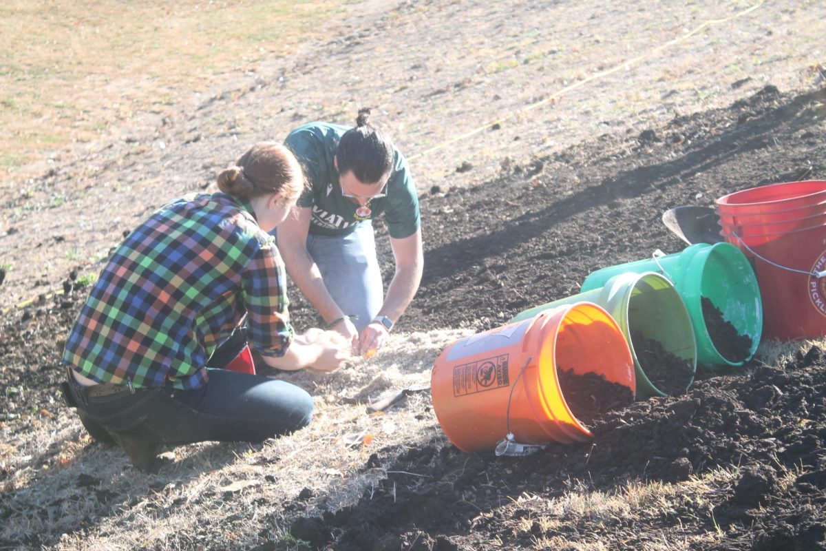 Darrow Center and Ryan pick up a chunk of spilled seeds for prairie plants that were being mixed to be distributed in five gallon buckets.