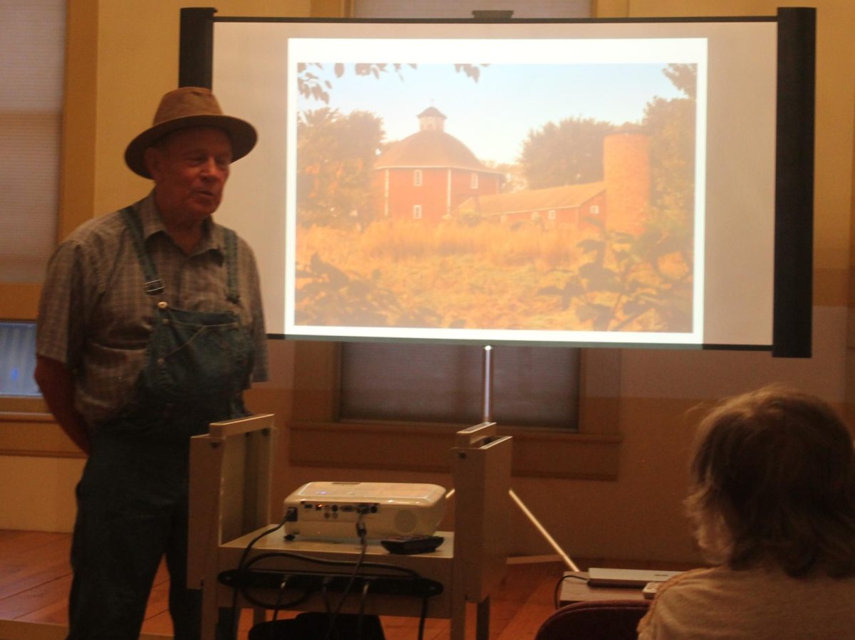 Rich Tyler alongside a painting of the Secrest Octagonal Barn he helped preserve and restore.