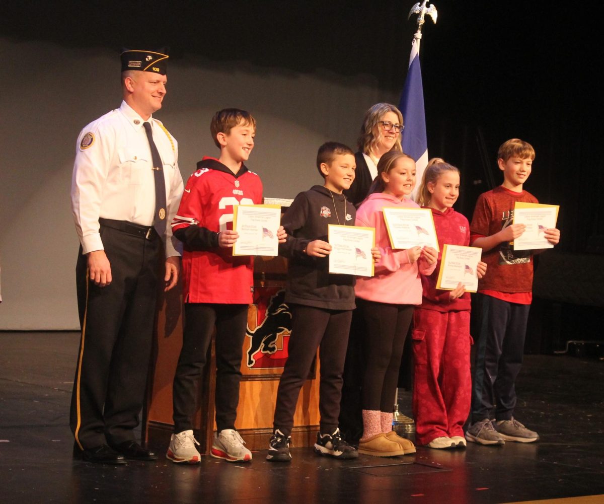 (From left) Lisbon Legion commander Brent Mollenhauer with essay winners Beckam Horman, Briggs Hofmeister, Charlee Wallace, teacher Chalupa (in back row) Annika Stensland and Damon Phillips at the ceremony Monday, Jan. 12.
